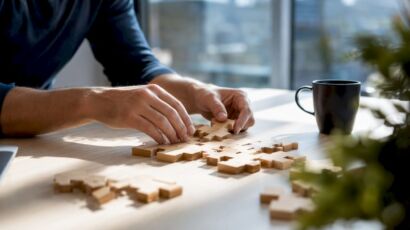 Hände setzen einzelne Puzzleteile auf einem Schreibtisch zusammen.